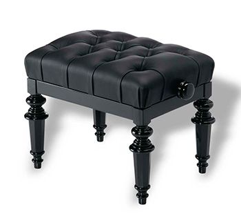 A black ottoman with tufted top and turned legs.